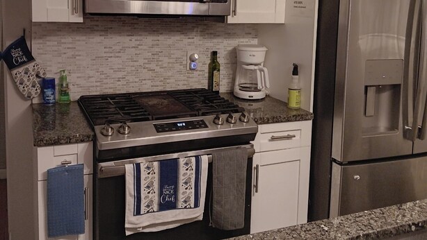 A kitchen with white cabinets, stainless steel appliances including a microwave and refrigerator, a gas stove, and a coffee maker.