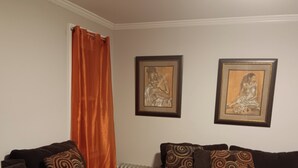 A living room with a brown sofa, a blue sofa, and an ottoman. There are two framed pictures on the wall.