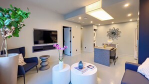 A modern living room with a sofa, two round coffee tables, a TV, and a dining area with a table and chairs.