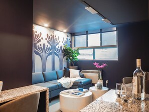 Uma sala de estar moderna com um sofá azul, uma mesa de centro e uma janela grande com vista para a cidade.
