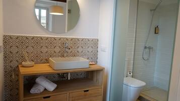 A bathroom with a wooden vanity, a round mirror, patterned tiles, a shower enclosure, and a toilet.