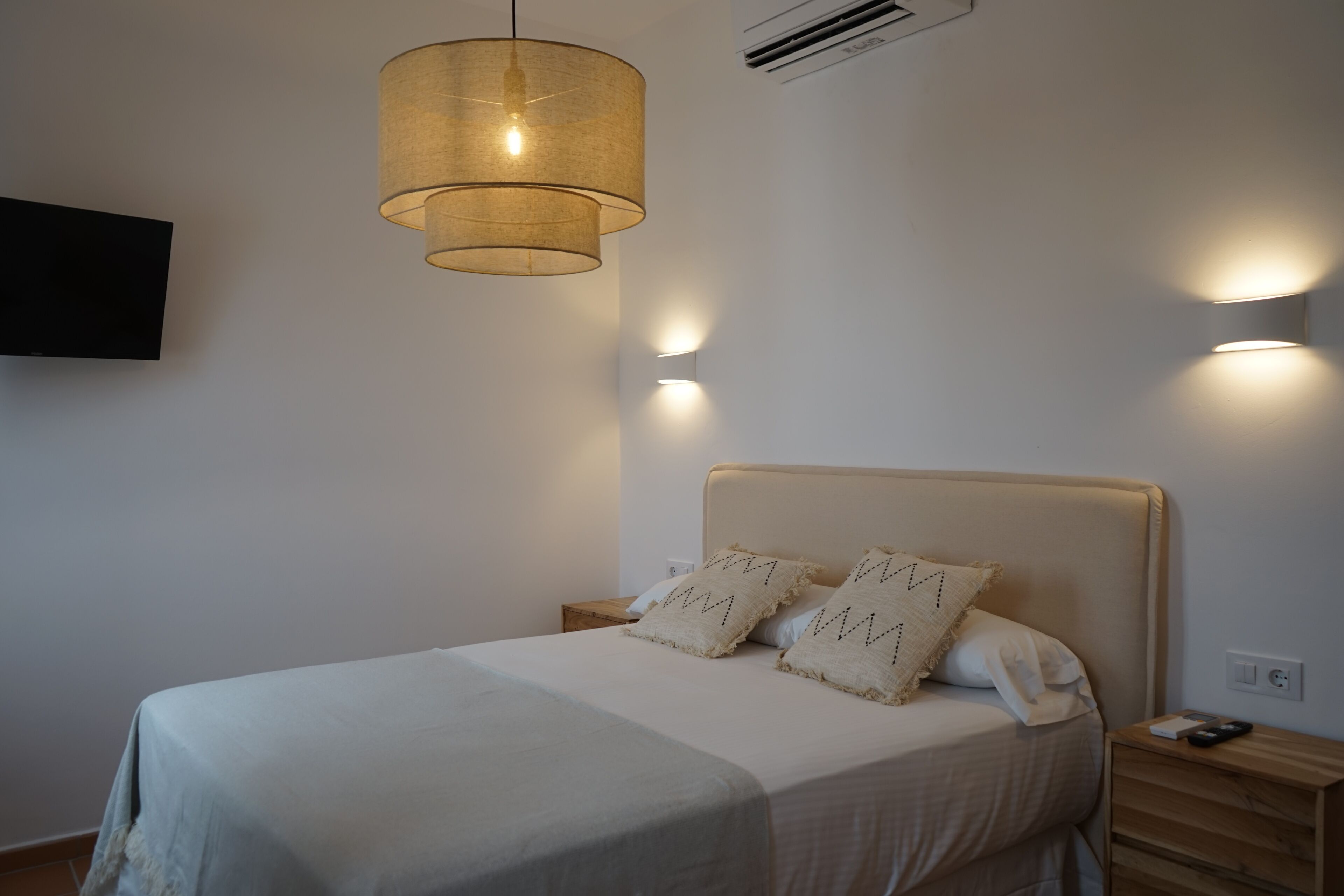 A neatly made bed with a headboard, two bedside tables, and a wall-mounted TV.