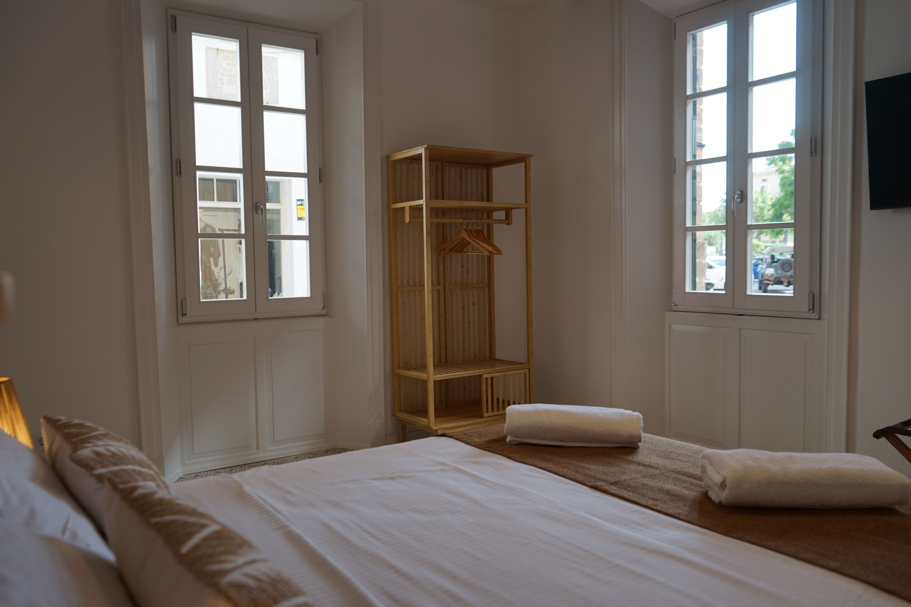A hotel room with a large bed, a wooden wardrobe, and a window with a view of the street.