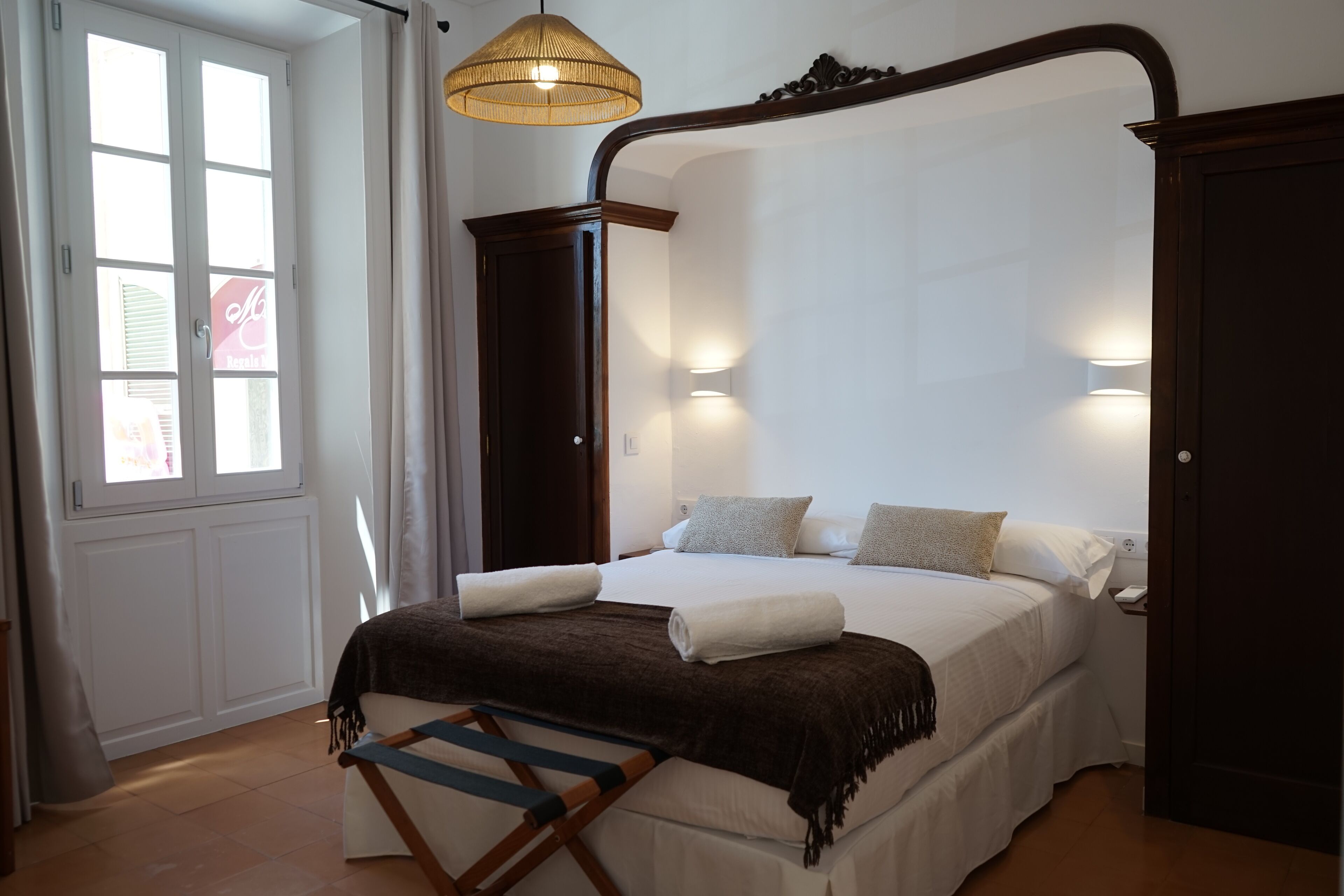Quarto com cama de dossel, escada de madeira, janela com cortinas e luminária fixa na parede.