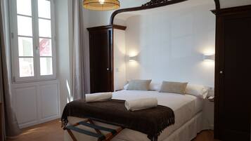 Quarto com cama de dossel, escada de madeira, janela com cortinas e luminária fixa na parede.