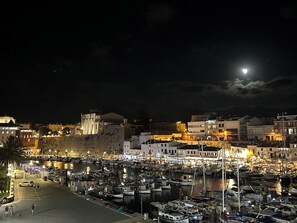 A nighttime marina with boats docked, a historic building with arches, and a moon in the sky. - Es Mirador Hotel (Ciutadella de Menorca)