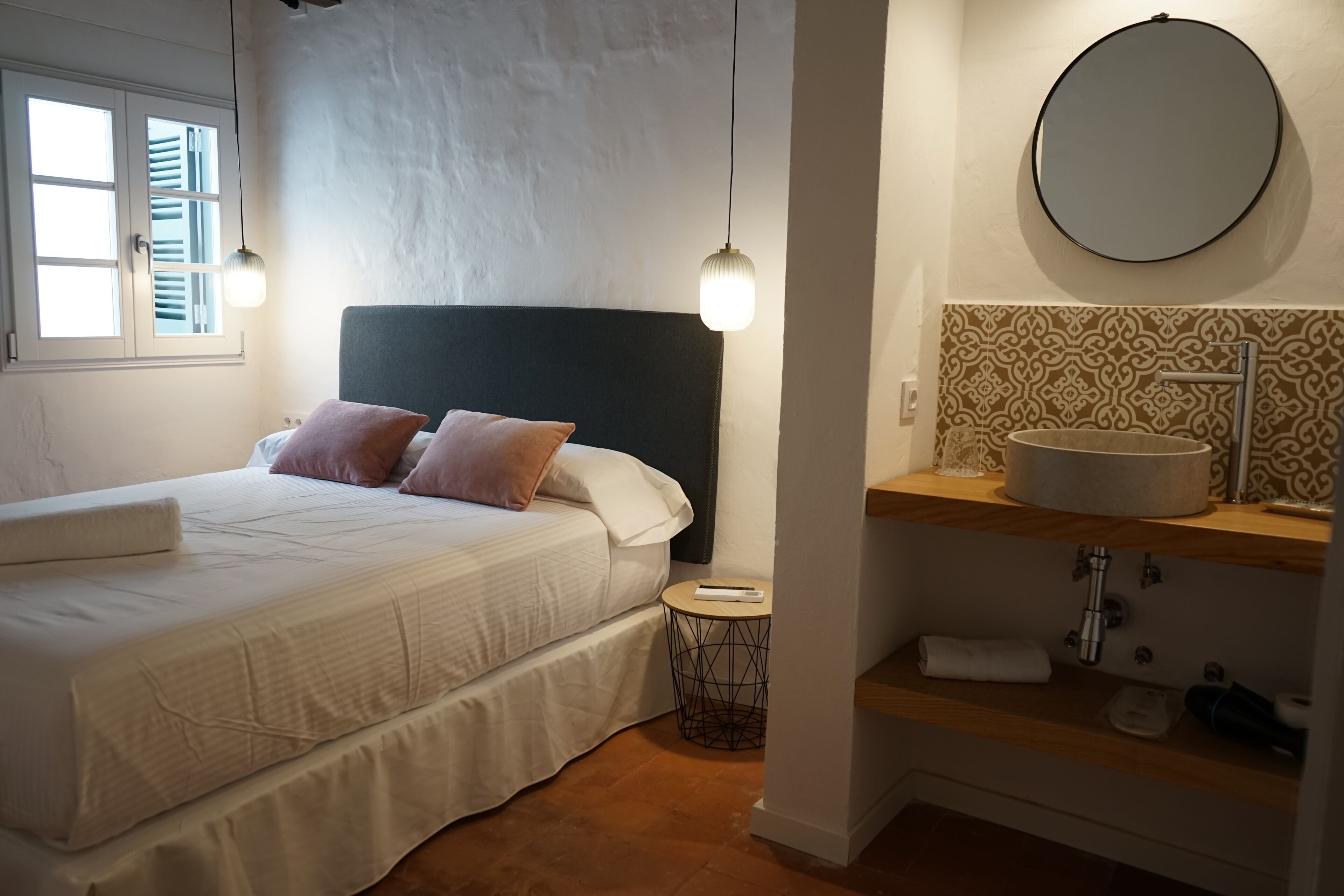 Une chambre à coucher avec un lit, une table de chevet et un miroir rond au-dessus d’un lavabo.