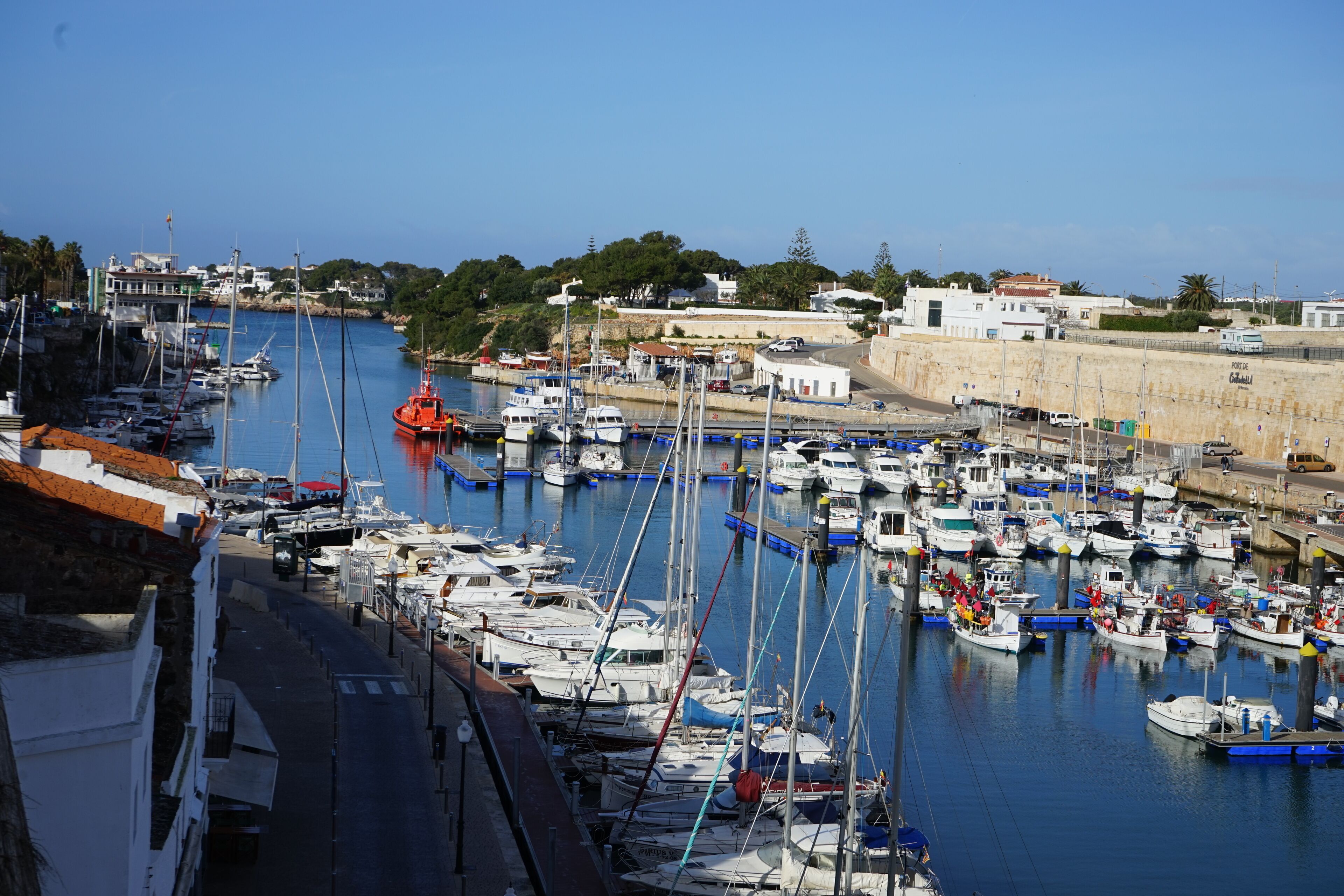 A marina with numerous boats docked, a clear sky, and buildings in the background.