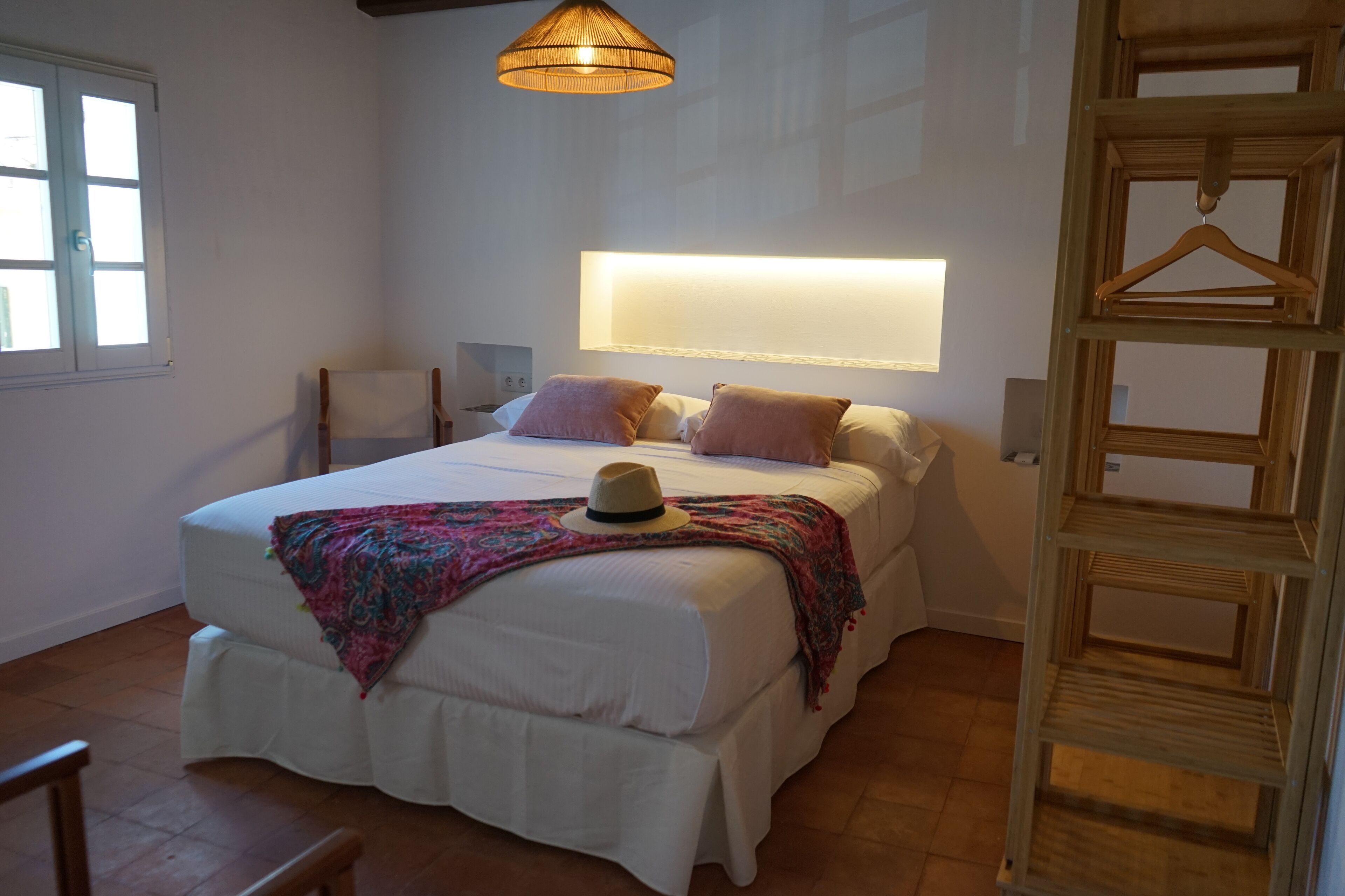 A bedroom with a large bed, bedside tables, a hanging light fixture, and a wooden wardrobe.