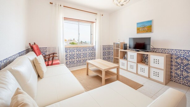 Una sala de estar con un sofá blanco, una mesa de centro de madera, un mueble para TV con televisor de pantalla plana y un salpicadero de azulejos estampados.