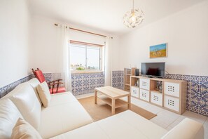 A living room with a white sofa, a wooden coffee table, a TV stand with a flat-screen TV, and a patterned tile backsplash. - GuestReady - Floral Ericeira residence (Mafra)