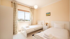 Habitación de hotel con dos camas, una ventana con cortinas, una mesita de noche con lámpara y un cuadro en la pared.