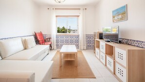 Una sala de estar con un sofá, un sillón rojo, una mesa de centro de madera, un televisor y una ventana con cortinas.