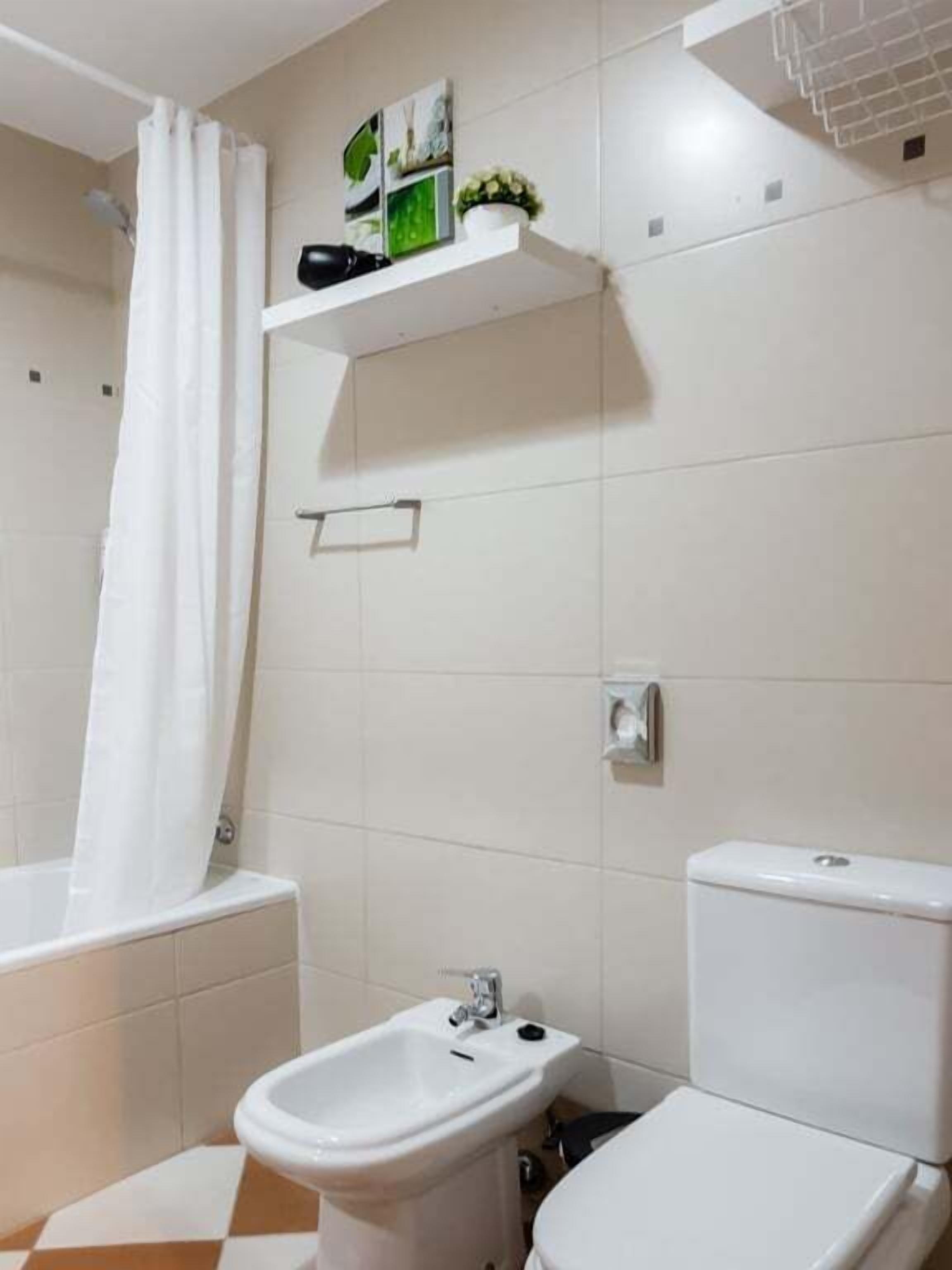 Une salle de bain équipée d’une baignoire, d’un bidet, de toilettes et d’une étagère où sont disposés des objets décoratifs.