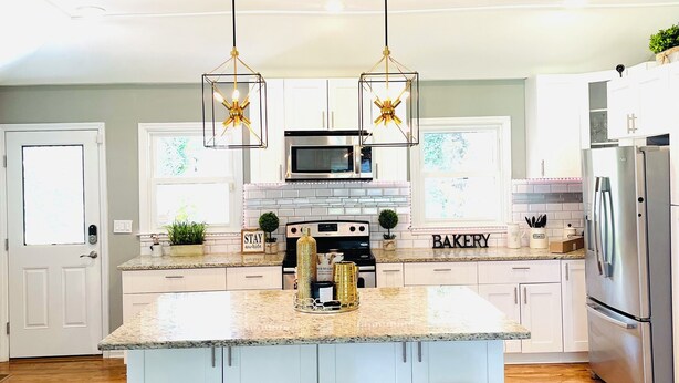 A modern kitchen with a central island, bar stools, stainless steel appliances, and pendant lighting. - Cozy Mid Century Modern Home Near Downtown (East Point)