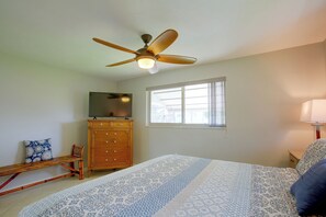Un dormitorio con cama, televisión, cómoda de madera, ventana y ventilador de techo.