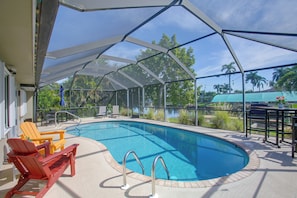 A covered outdoor swimming pool with a clear view of the surrounding greenery and a distant body of water. - Private Dock & Lanai: Waterfront Cape Coral Home! (Cape Coral)