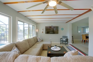 A spacious living room with a large sectional sofa, a flat-screen TV mounted on the wall, and a ceiling fan. - Private Dock & Lanai: Waterfront Cape Coral Home! (Cape Coral)
