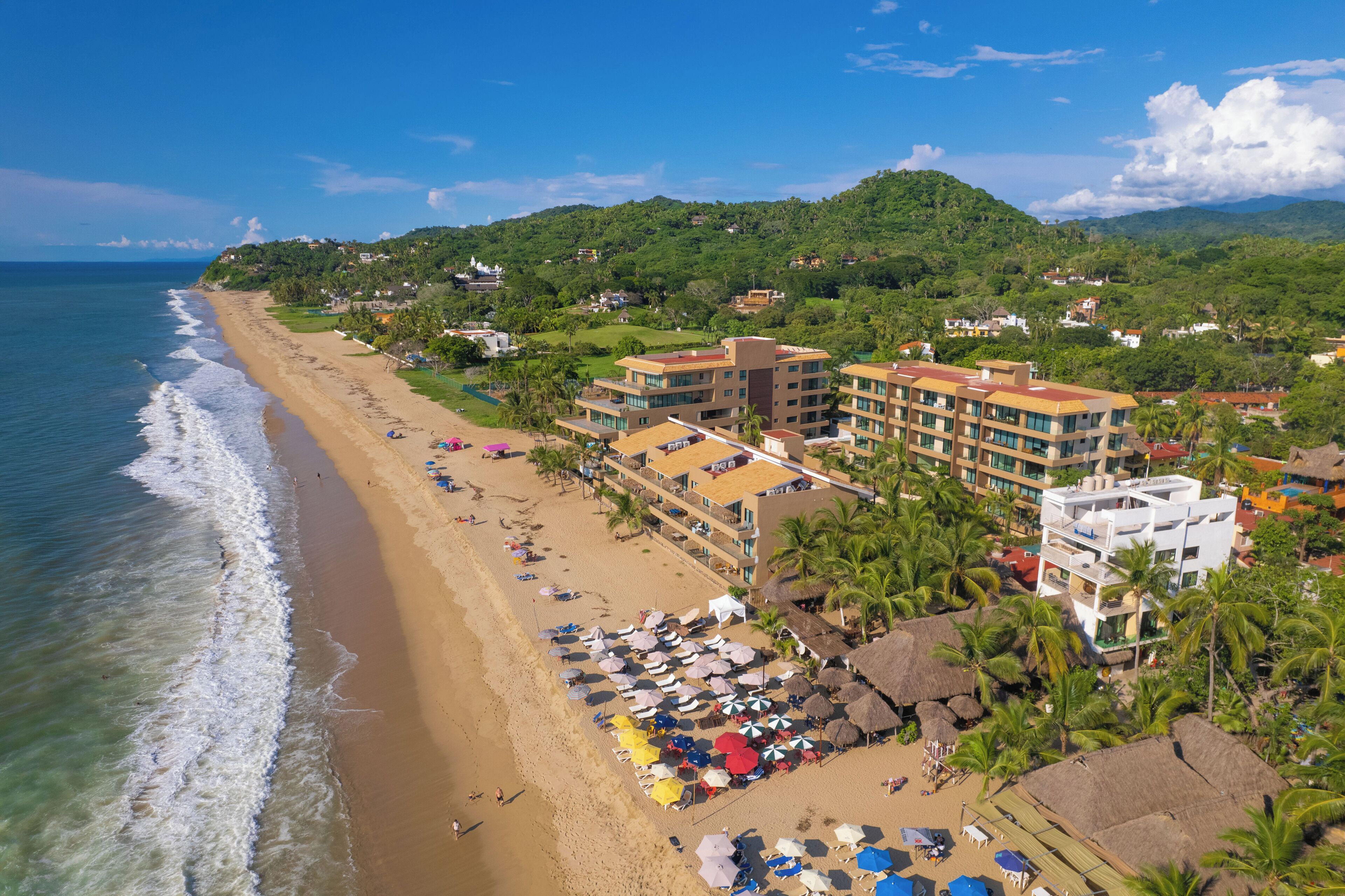 A beach resort with multiple buildings, a sandy beach, and palm trees.