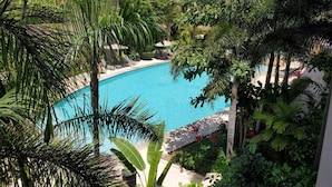 A swimming pool surrounded by lush greenery and palm trees, with a building in the background. - Villa Dahlia Estudio a metros del mar (San Francisco)
