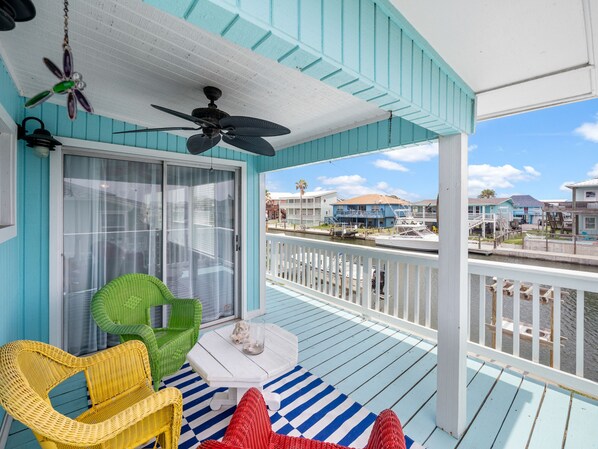 A covered porch with a view of a marina, featuring a ceiling fan, wicker chairs, and a striped rug. - Off the Charts by Miss Kitty’s (Aransas Pass)