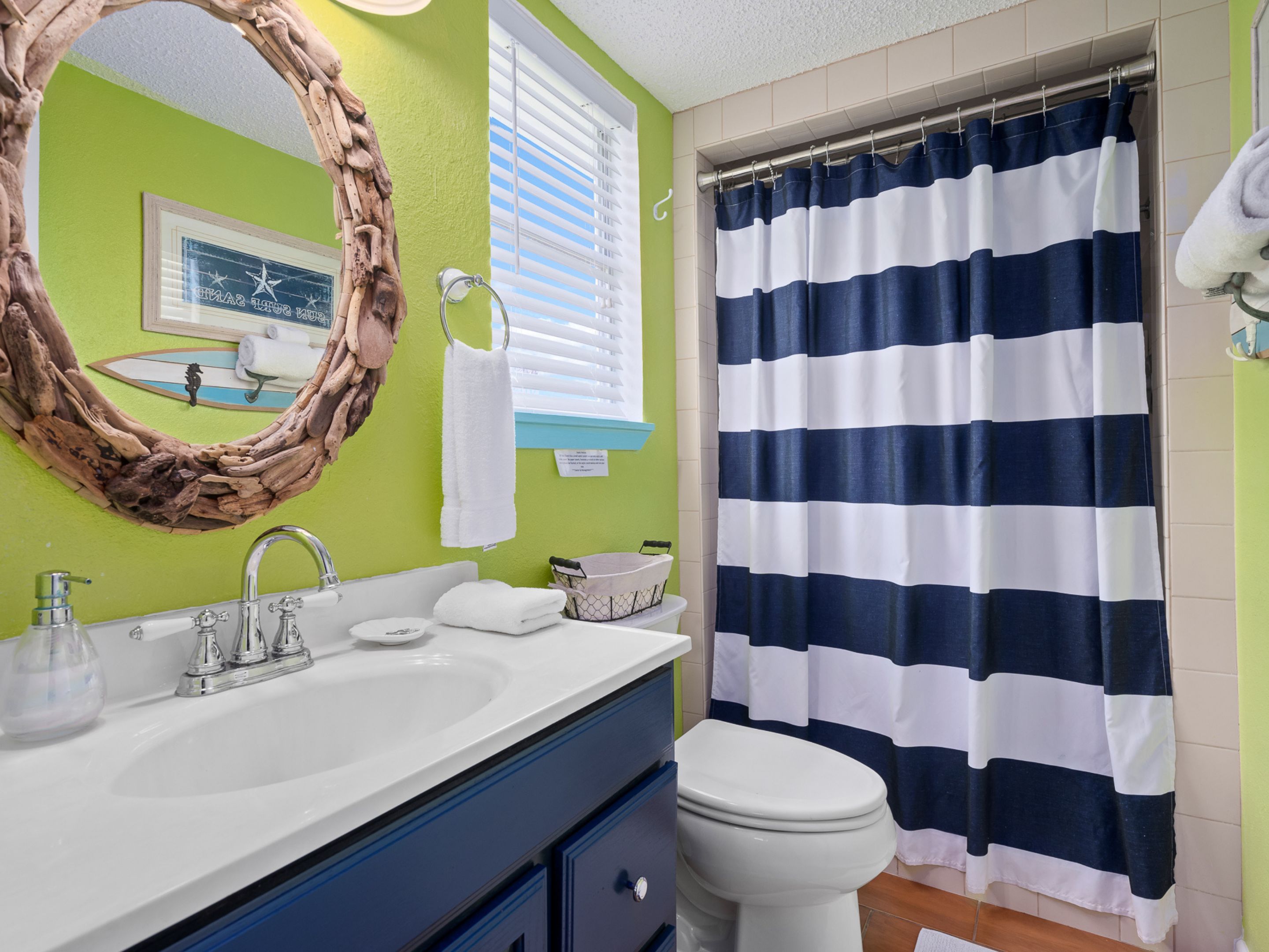 A bathroom with a white sink, a large mirror, a toilet, and a striped shower curtain.
