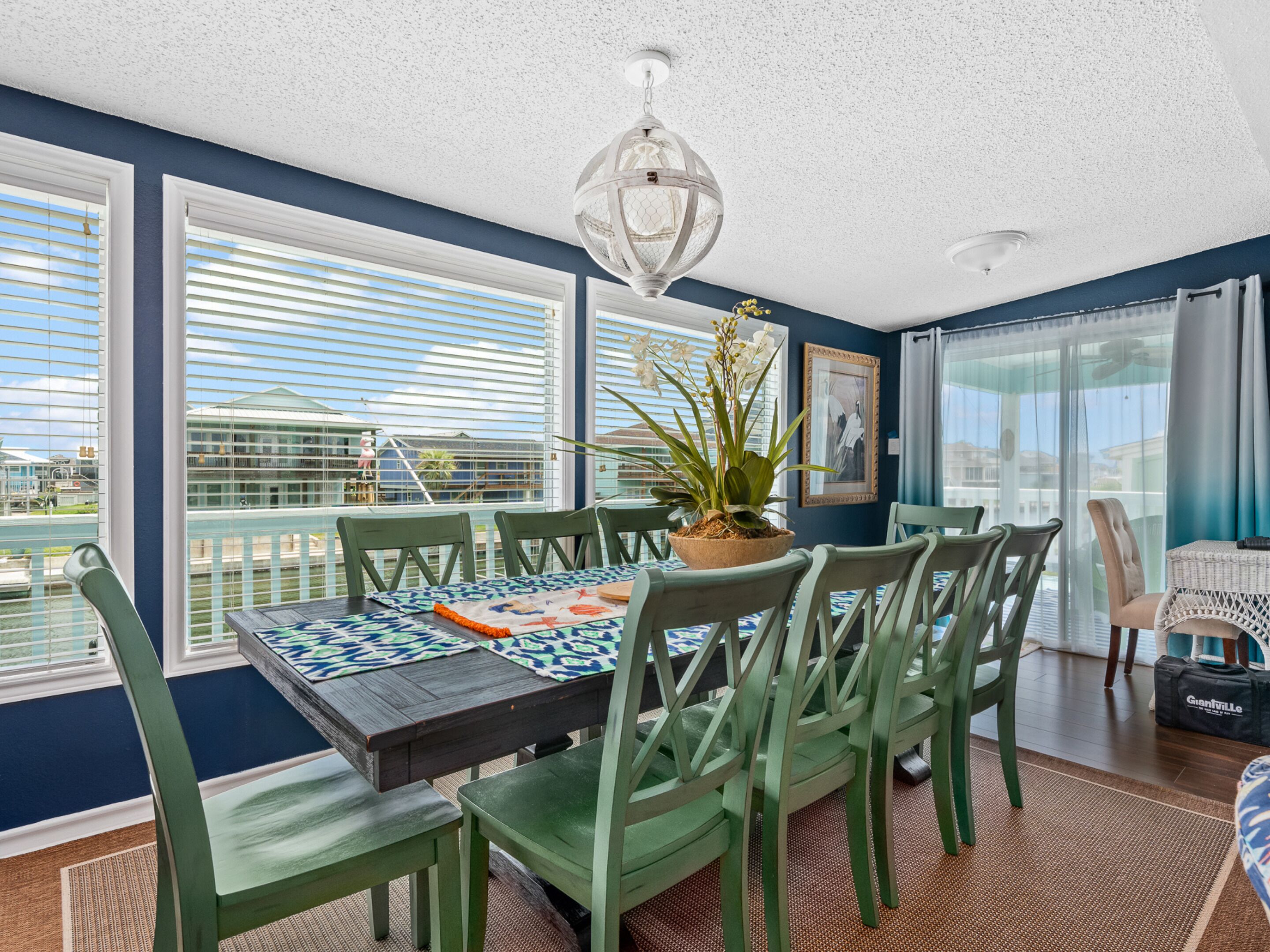 A dining area with a table set for six, surrounded by green chairs, a potted plant, and a decorative ceiling light.