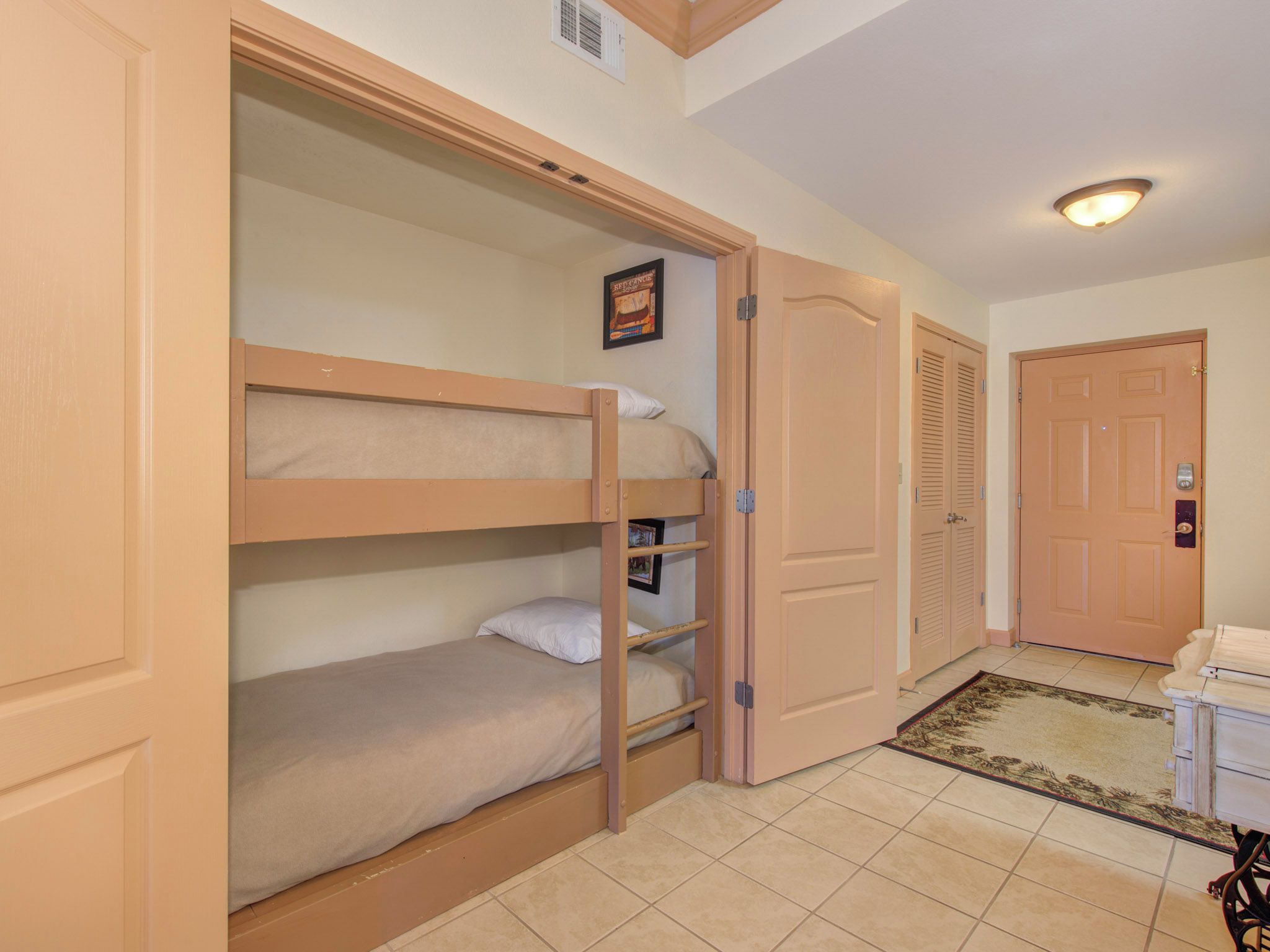 A room with a bunk bed, a door, a small desk, and a rug.