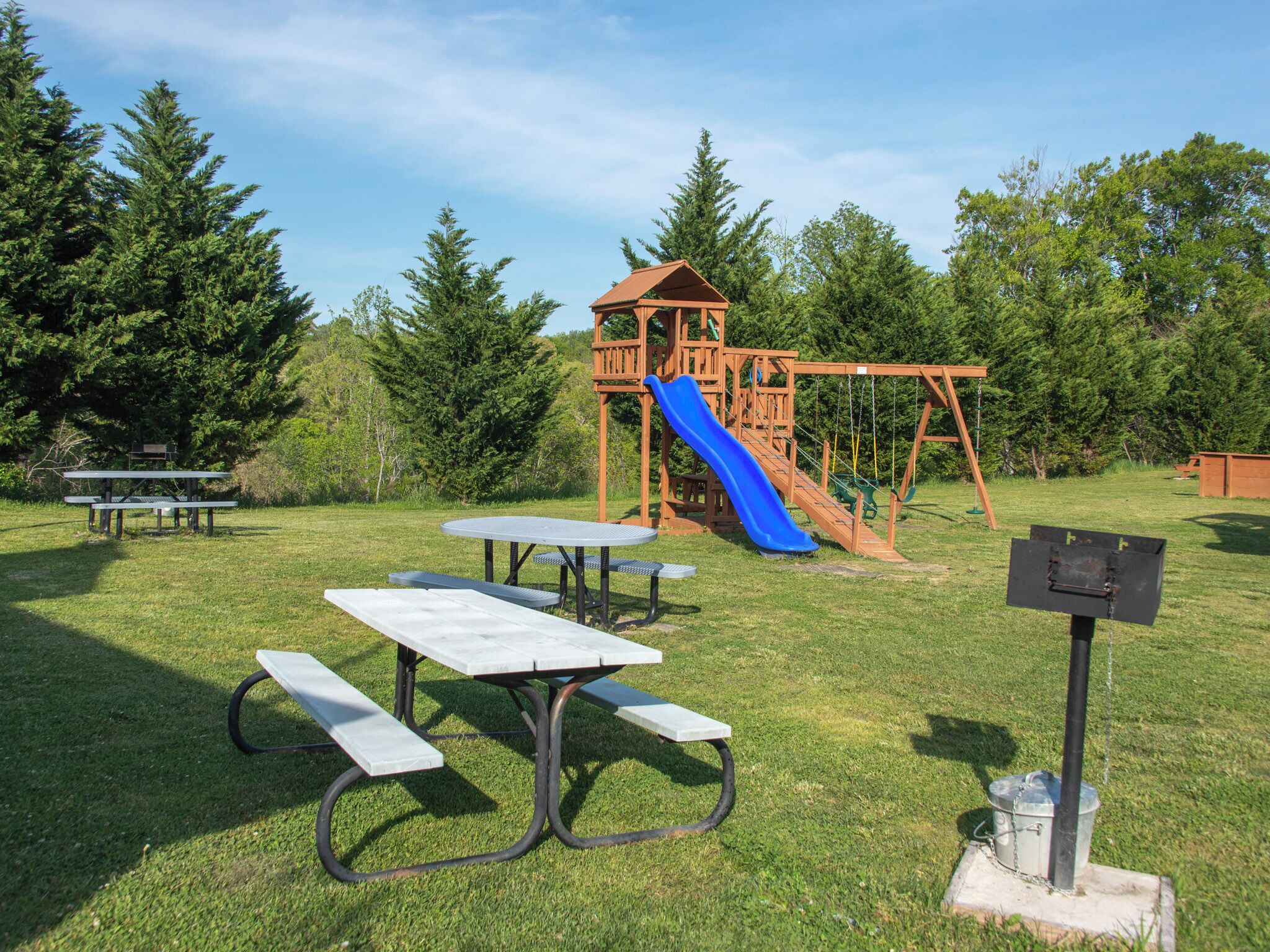 A playground with a slide and swings, picnic tables, and a wooden playhouse.