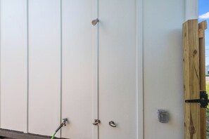 A white exterior wall with a wooden door frame, a metal door handle, and a small electrical box. - Chillin at the Beach by Silver Sands Vacation Rentals (Port Aransas)