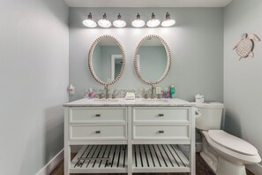 A bathroom with a white vanity, two oval mirrors with bead trim, a toilet, and a wall-mounted towel rack. - Chillin at the Beach by Silver Sands Vacation Rentals (Port Aransas)