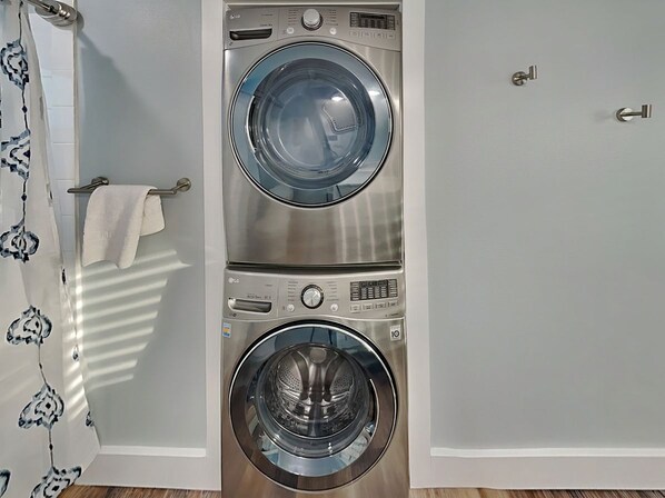 A compact washer and dryer unit in a bathroom with a towel rack and a door lock. - Chillin at the Beach by Silver Sands Vacation Rentals (Port Aransas)