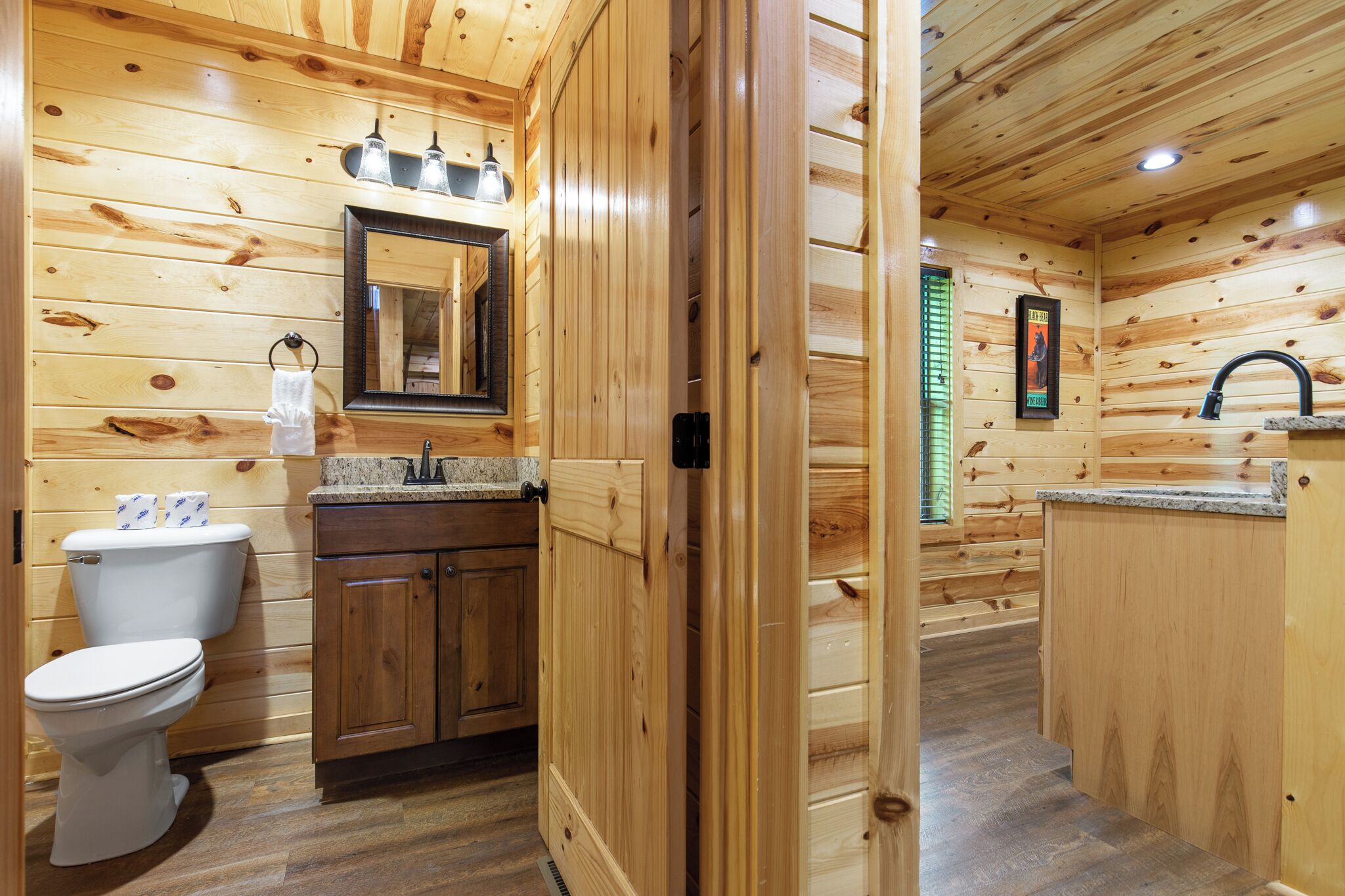 A wooden cabin bathroom with a toilet, sink, and mirror.