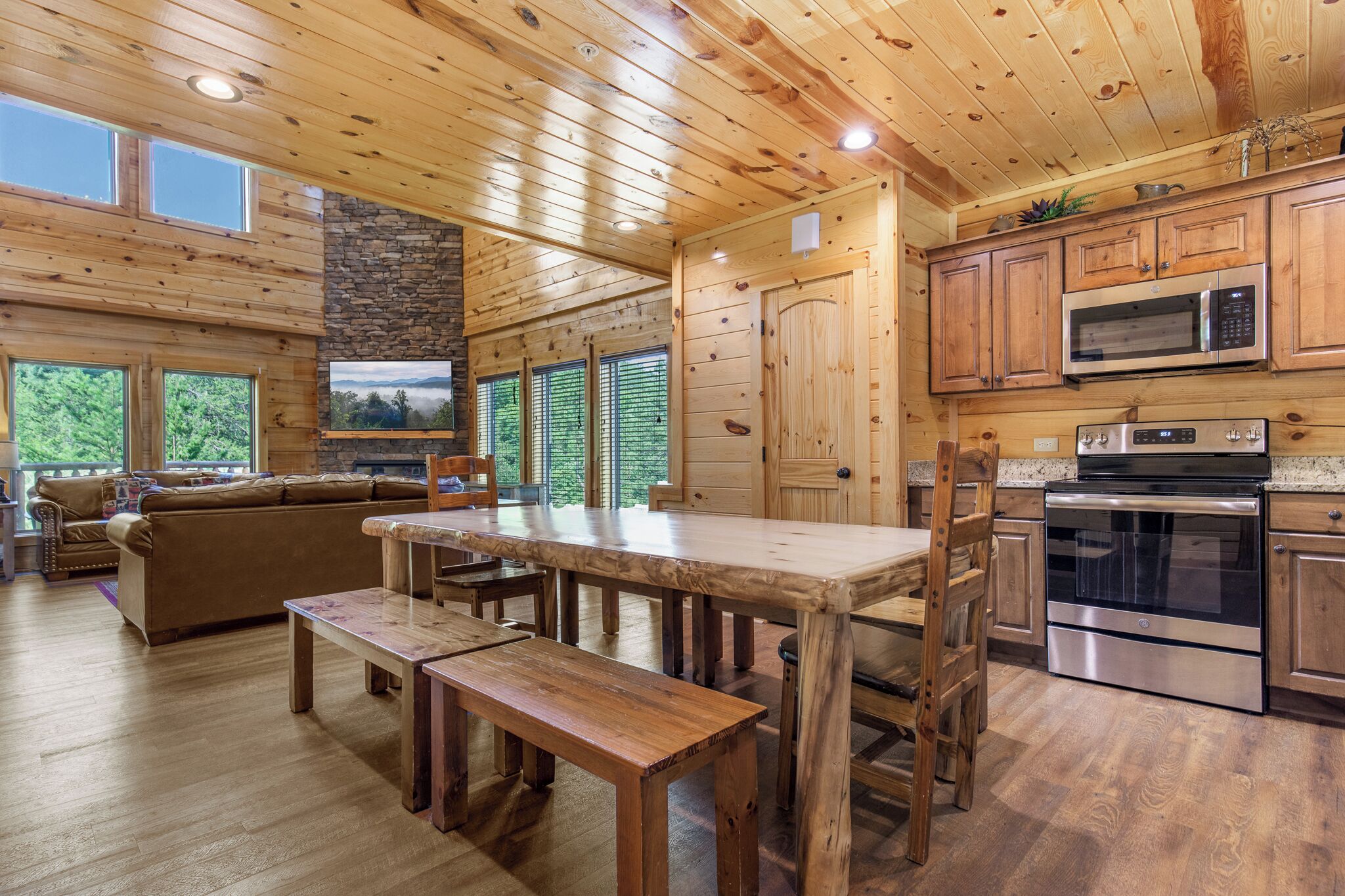 L’intérieur d’un chalet en bois comprend une table à manger, des bancs, un canapé et un coin cuisine équipé d’appareils électroménagers modernes.