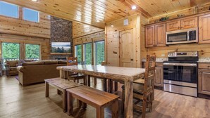 A wooden cabin interior with a dining table, benches, a sofa, and a kitchen area with modern appliances. - Mountain High Cinema by Jackson Mountain Rentals (Sevierville)