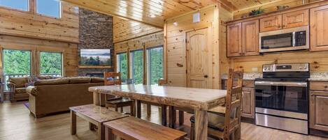 L’intérieur d’un chalet en bois comprend une table à manger, des bancs, un canapé et un coin cuisine équipé d’appareils électroménagers modernes.