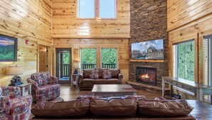 A cozy cabin interior with a fireplace, leather sofas, and a stone accent wall. - Mountain High Cinema by Jackson Mountain Rentals (Sevierville)