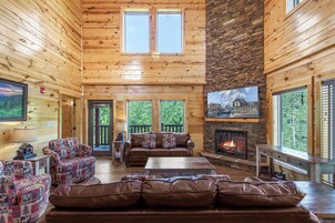 A cozy cabin interior with a fireplace, leather sofas, and a stone accent wall.