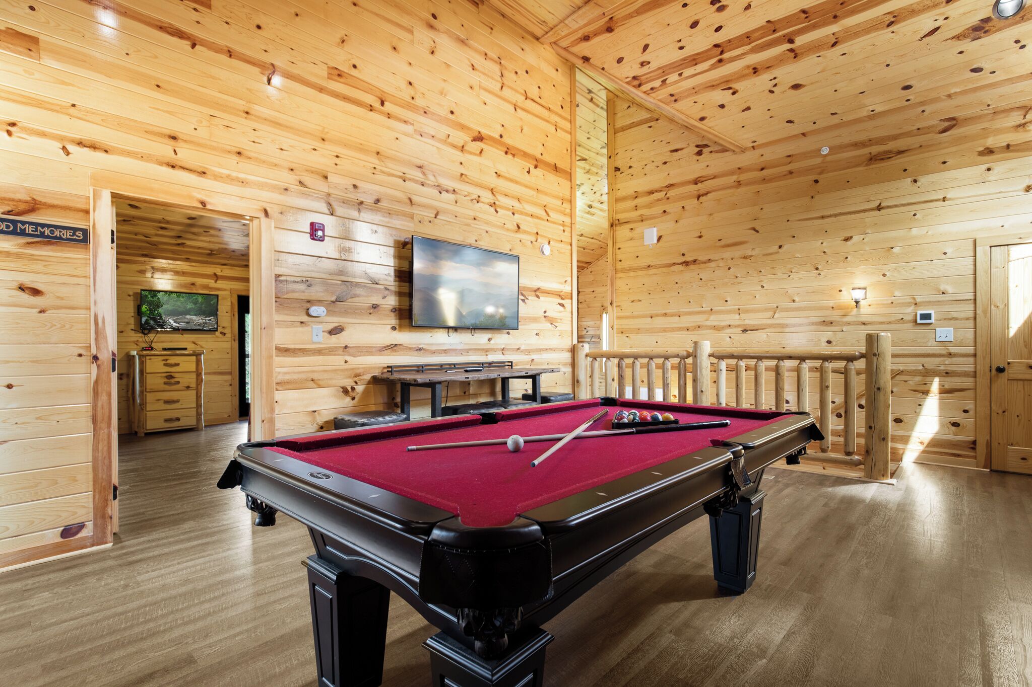 A wooden interior with a pool table, a television, and a wooden railing.