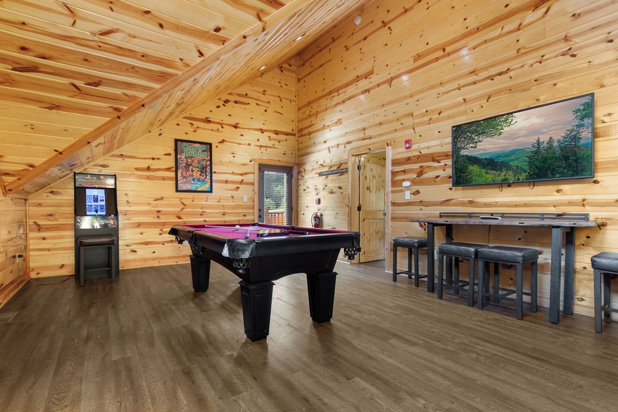 A wooden interior with a pool table, bar area, and a large TV screen.