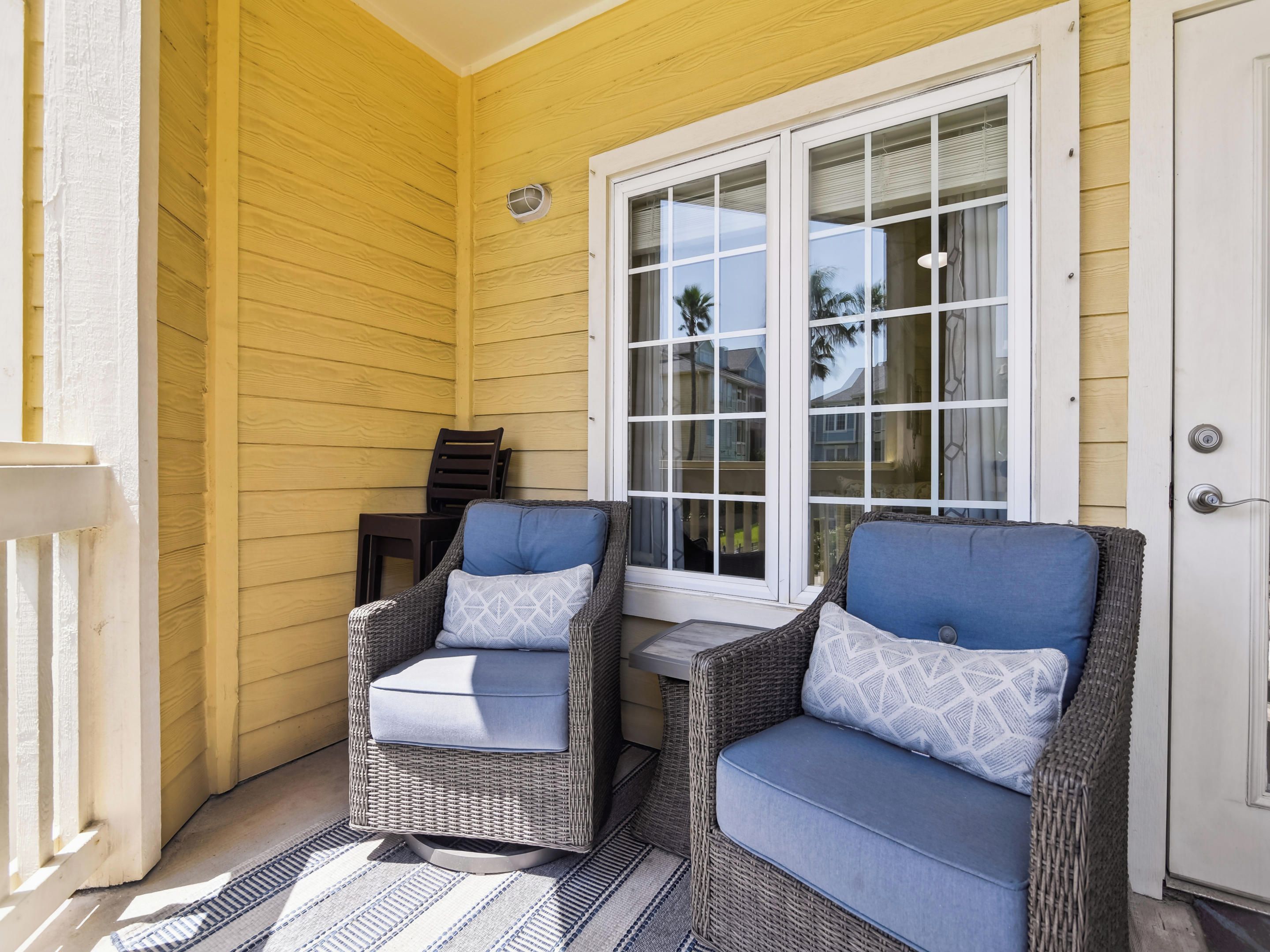 A porch with two wicker chairs, a small table, and a window with blinds.