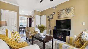 A living room with a sofa, armchairs, a coffee table, a TV, and a dining area in the background. - Beach Daze by Ryson Vacation Rentals (Galveston)