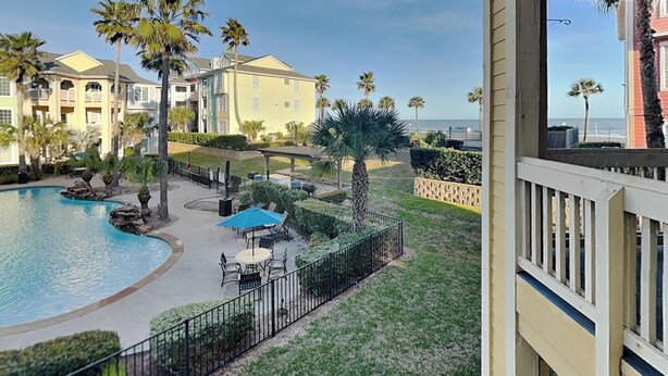 A pool area with palm trees, outdoor seating, and a view of the ocean. - Beach Daze by Ryson Vacation Rentals (Galveston)