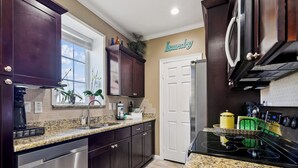 A modern kitchen with dark wood cabinets, a granite countertop, stainless steel appliances, and a 'Laundry' sign on the wall. - Beach Daze by Ryson Vacation Rentals (Galveston)