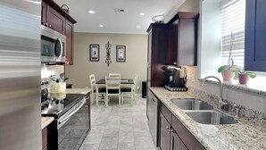 A kitchen with granite countertops, stainless steel appliances, and a dining area with a table and chairs. - Beach Daze by Ryson Vacation Rentals (Galveston)