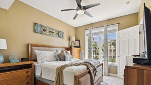 A bedroom with a bed, bedside table, lamp, and a view of the outside through a window. - Beach Daze by Ryson Vacation Rentals (Galveston)