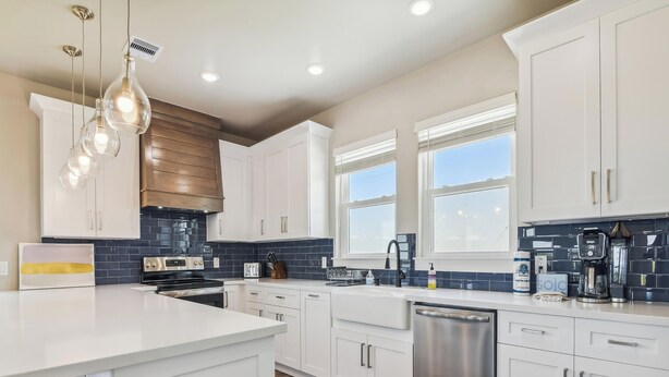 A modern kitchen with white cabinets, a stainless steel dishwasher, a built-in oven, and a large island with bar stools. - Bayfront Nirvana! by Ryson Vacation Rentals (Galveston)