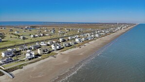 An aerial view of a coastal residential area with houses along the beach and a clear blue sky. - Bayfront Nirvana! by Ryson Vacation Rentals (Galveston)