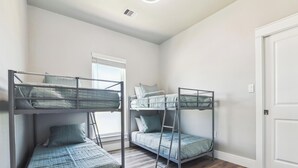 A room with two bunk beds, a window with blinds, a white door, and a wooden floor. - Bayfront Nirvana! by Ryson Vacation Rentals (Galveston)