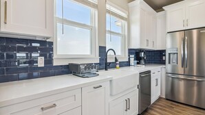 A modern kitchen with white cabinets, a stainless steel refrigerator, and a blue-tiled backsplash. - Bayfront Nirvana! by Ryson Vacation Rentals (Galveston)